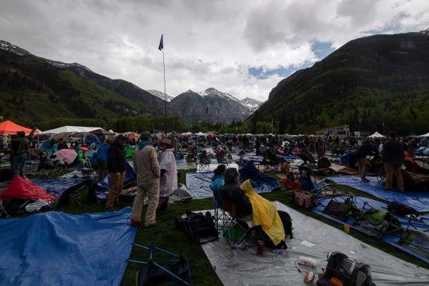 Attendees of the 50th Telluride Bluegrass Festival huddle under rain gear as rainstorms move through the San Juan Mountains overlooking Town Park in Telluride, Colo., during the opening day of the festival Thursday, June 15, 2023. (William Woody, Special to The Denver Post)